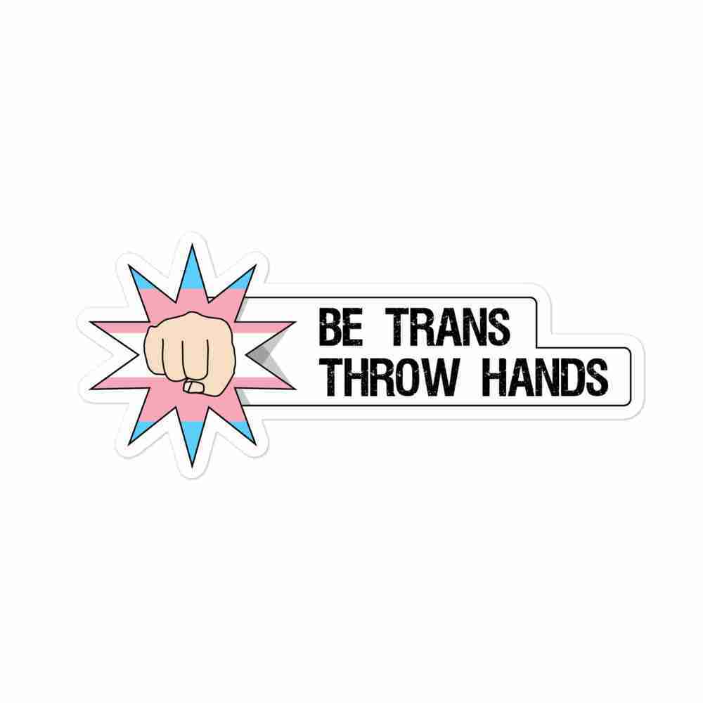 A sticker of a first punching through a white backdrop to reveal a trans flag, with text to the right reading "Be trans, throw hands".